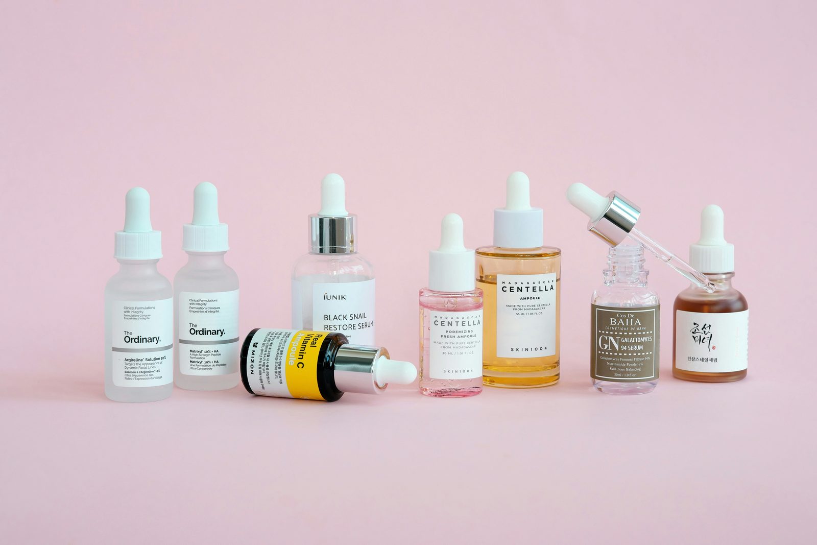 Rij Koreaanse serums en ampullen met centella, snail mucin en galactomyces op een roze achtergrond
