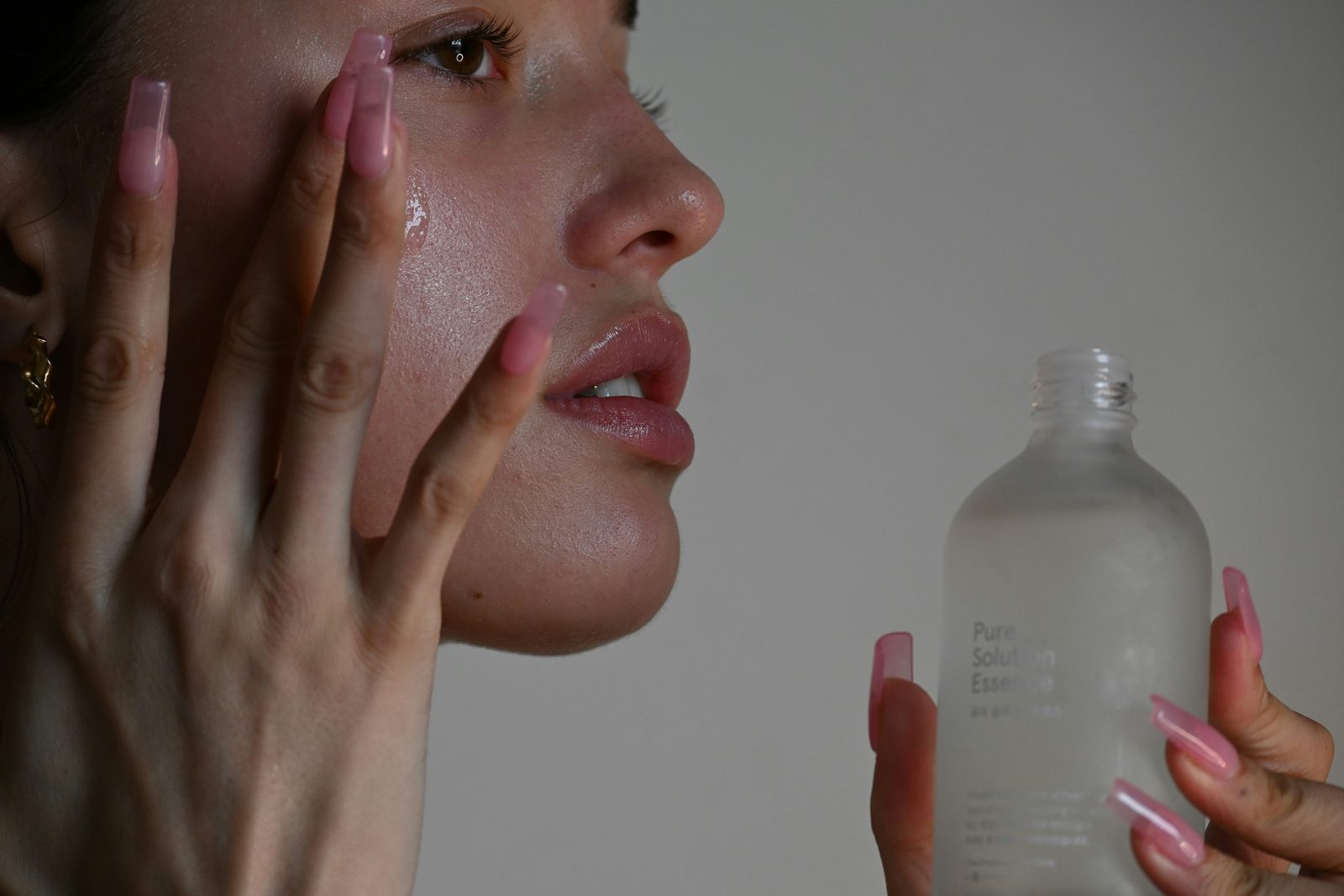 Close-up van een vrouw die met haar vingertoppen een essence op haar vochtige huid tikt, naast een flesje essence