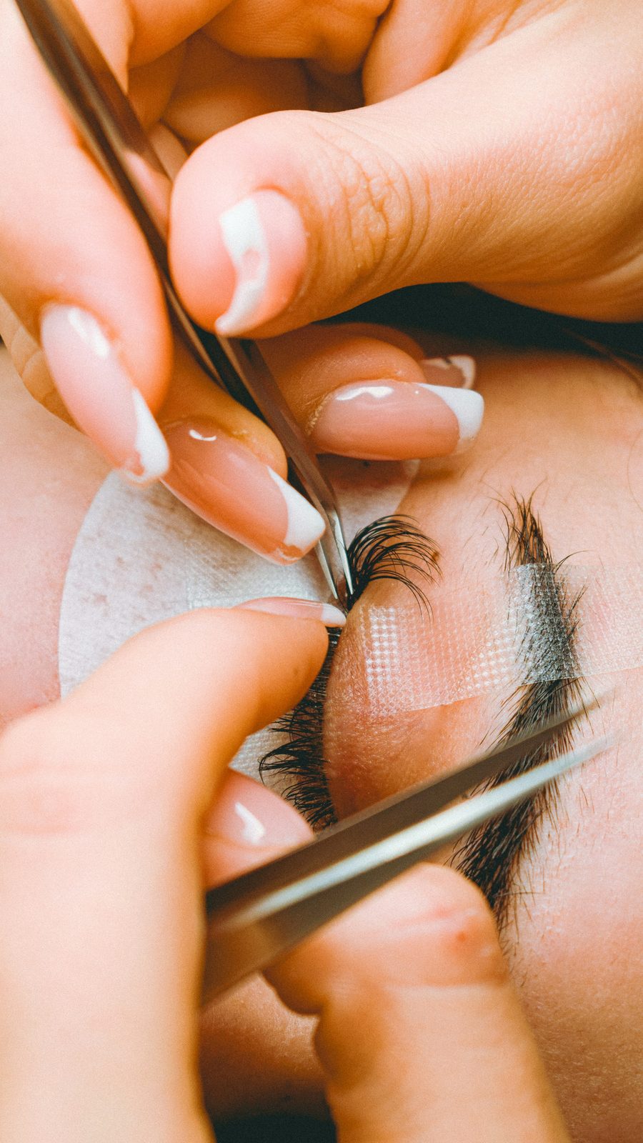 Wimperstylist brengt nauwkeurig een extension aan met twee pincetten