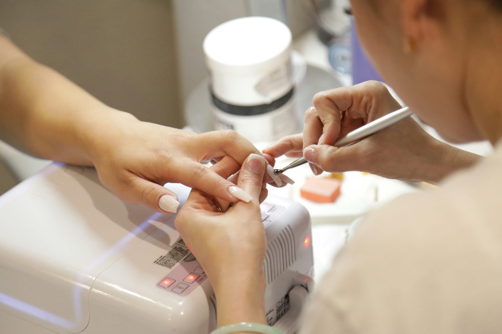 Nagelstyliste werkt met tools en een UV-lamp tijdens een nagelbehandeling