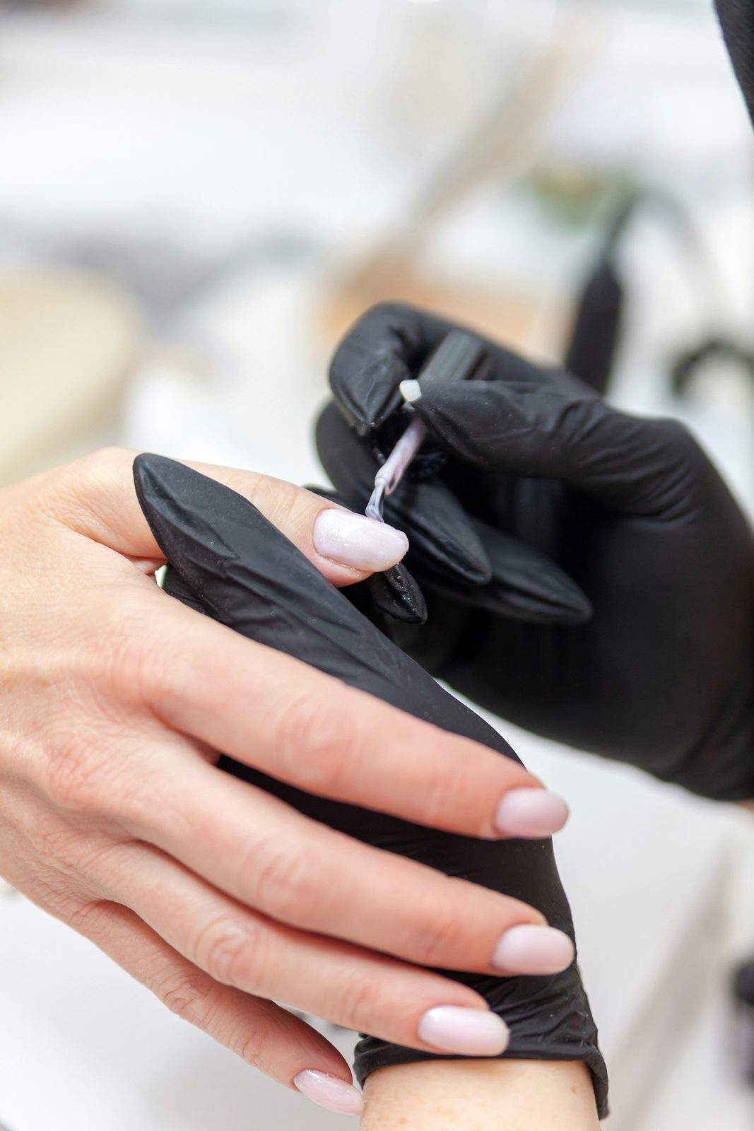 Nagelstyliste met handschoenen brengt gel aan tijdens een behandeling
