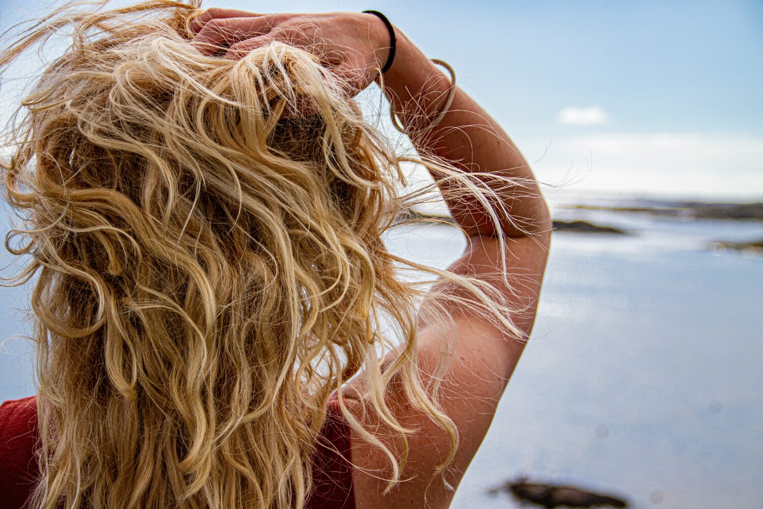 Blond, golvend haar met pluis en vliegende haartjes tegen een strandlucht