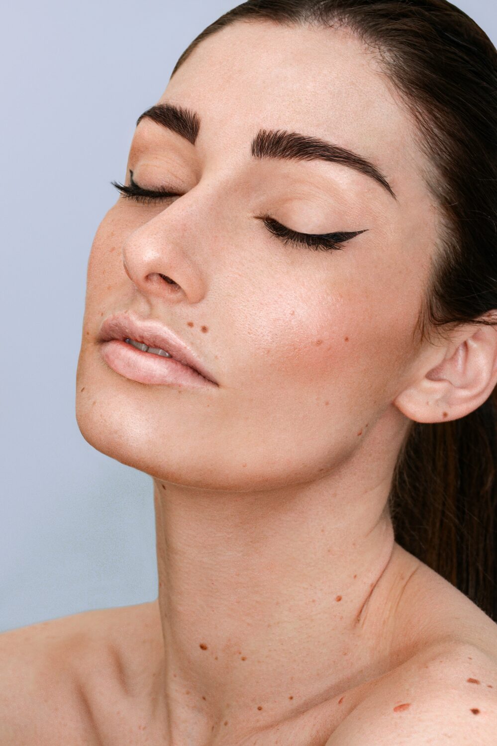 Vrouw met gesloten ogen en volle, natuurlijke donkere wenkbrauwen en strakke eyeliner