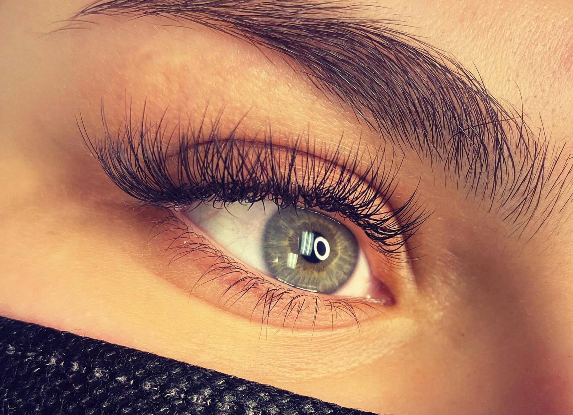 Close-up van een oog met volle, donkere wimperextensions en een verzorgde wenkbrauw