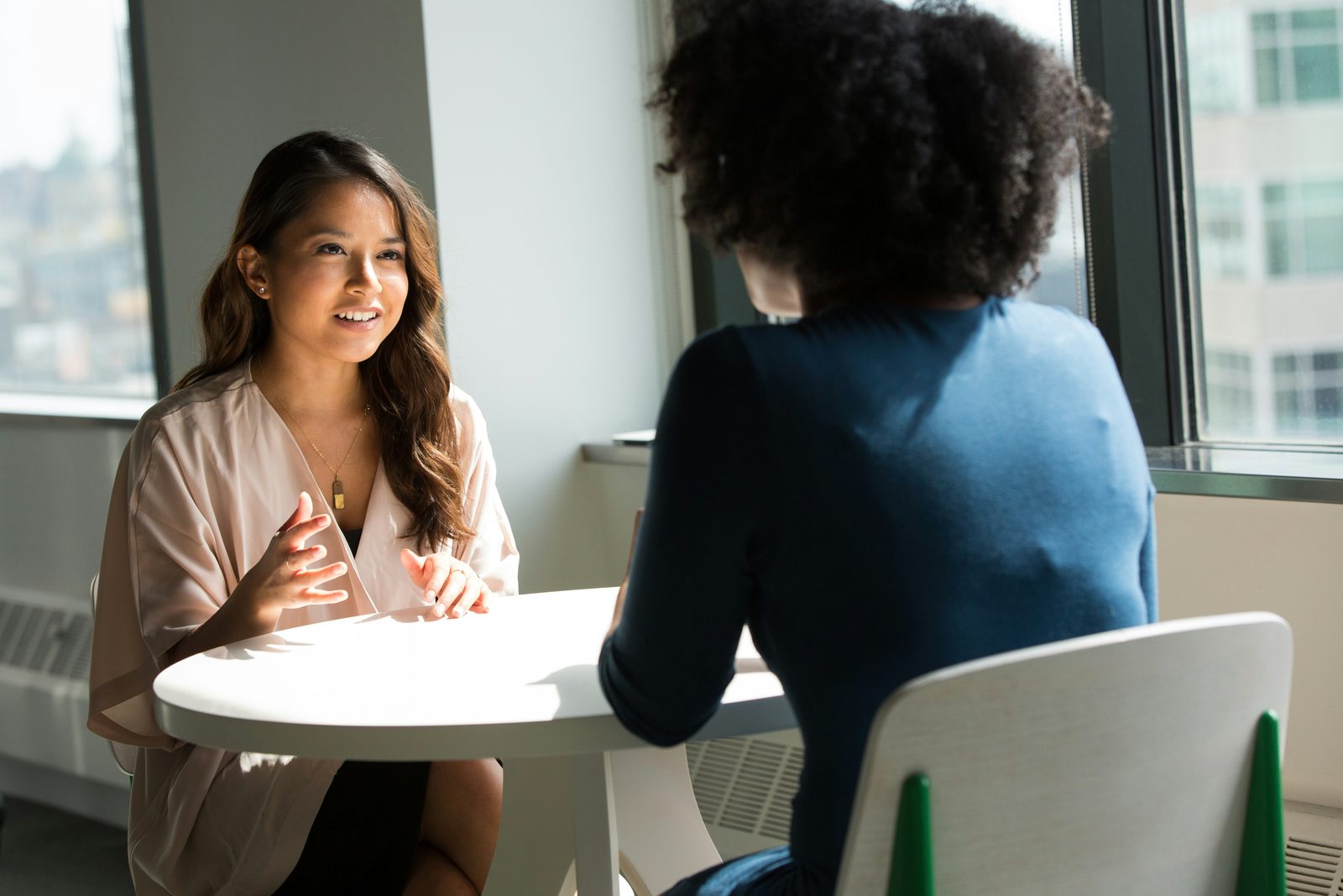 Twee vrouwen in gesprek aan een tafel bij het raam